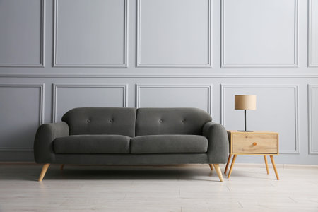 Stylish sofa and lamp on side table near gray wall