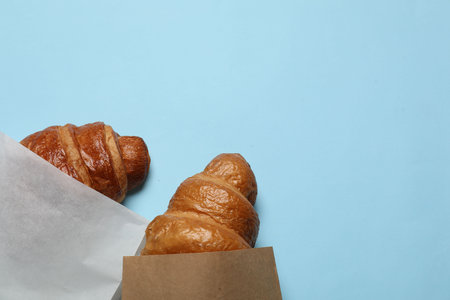 Paper bags with fresh croissants on light blue background, top view. Space for textの写真素材