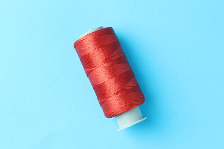 Spool of red sewing thread on light blue background, top view
