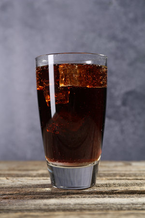 Sweet soda water with ice cubes in glass on wooden table