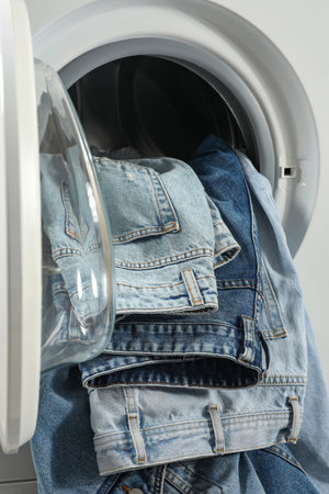 Washing machine with dirty jeans and other denim clothes indoors, closeup