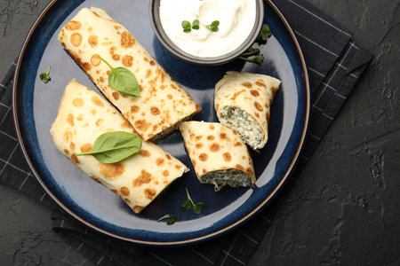 Delicious crepes with cottage cheese, spinach and sour cream on black table, top viewの写真素材