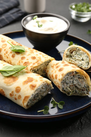 Delicious crepes with cottage cheese, spinach and sour cream on black table, closeupの写真素材