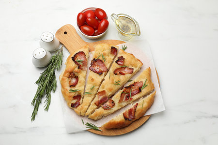 Slices of delicious focaccia bread with bacon, rosemary, oil and tomatoes on white marble table, flat layの写真素材