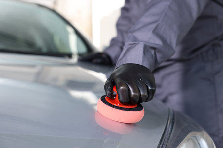 Man polishing car hood with sponge indoors, closeup