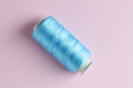 Spool of light blue sewing thread on pink background, top view