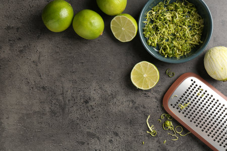 Lime zest, fresh fruits and grater on grey textured table. Space for textの写真素材