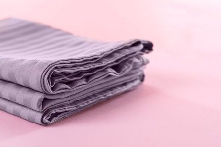 Stacked clean bed linens on pink background, closeup. Space for text