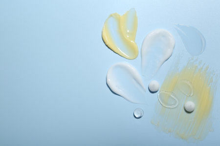 Cream and gel samples on light blue background, top view. Space for text