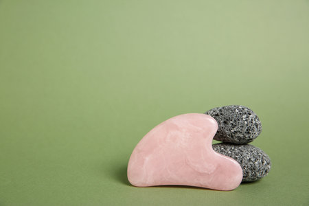 Gua sha tool and stones on green background. Space for text