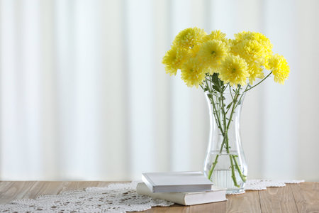 Beautiful yellow flowers in vase and books on wooden table at home. Space for textの写真素材