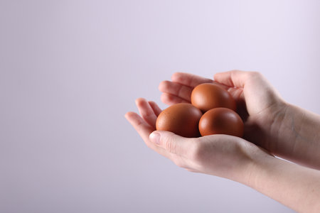 Woman with raw eggs on light background, closeup. Space for textの写真素材