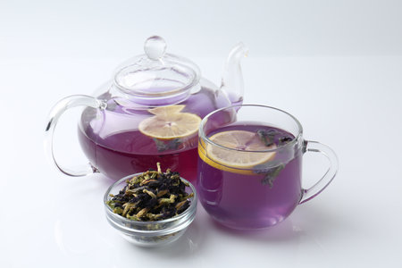 Delicious butterfly pea flower tea with lemon, teapot and dry petals on white tableの写真素材