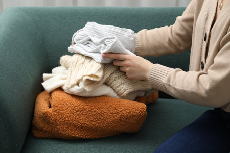 Woman stacking different used clothes on sofa indoors, closeup