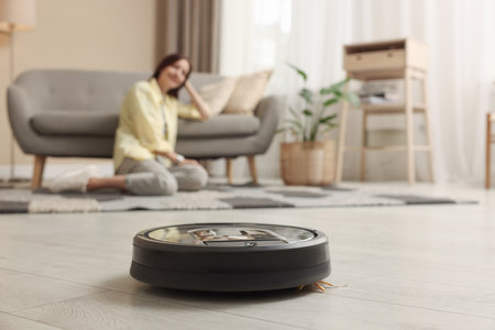 Young woman resting at home, focus on robotic vacuum cleanerの写真素材