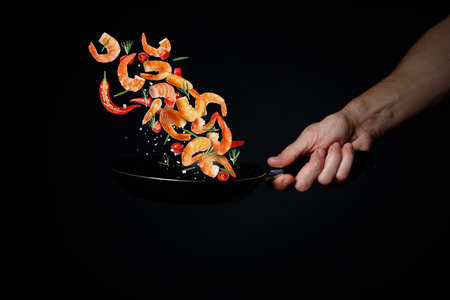 Chef cooking shrimps with chili pepper in frying pan on black background, closeupの写真素材