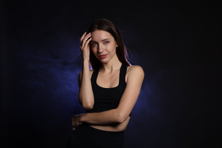 Beautiful woman in stylish sportswear on dark background with color lightの写真素材