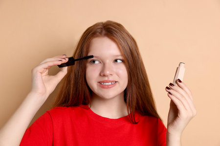 Smiling teenage girl applying mascara on beige backgroundの写真素材