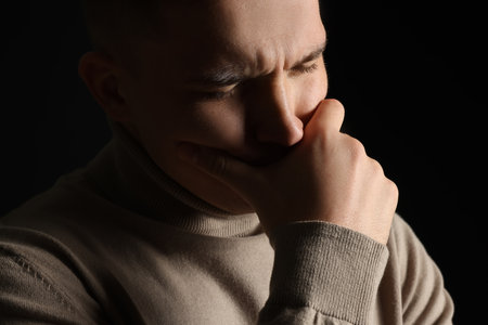 Distressed young man crying on black background, closeupの写真素材