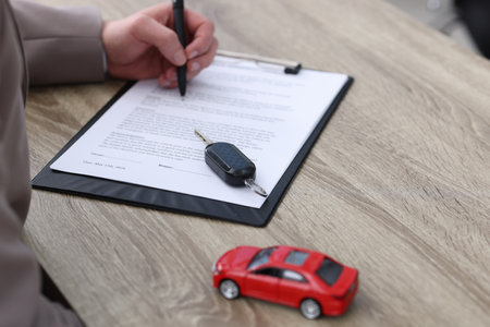Man signing car purchase agreement at wooden table, selective focus. Buying autoの写真素材