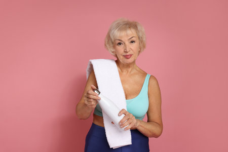 Senior woman with towel and water on pink backgroundの写真素材