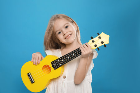 Little girl with ukulele on light blue backgroundの写真素材