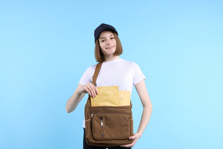 Happy woman with bag and envelopes on light blue background