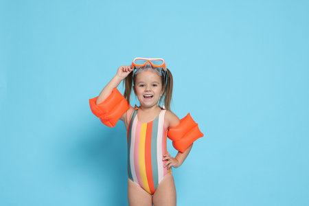 Cute little girl in swimsuit with swim armbands on light blue backgroundの写真素材