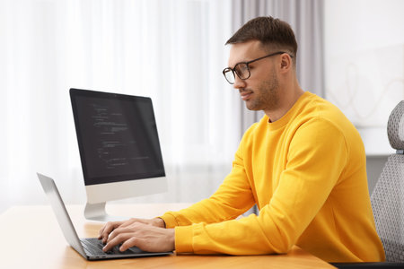 Programmer working on laptop at wooden desk indoors