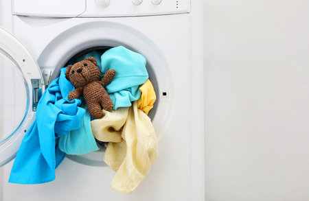 Washing machine with clothes and toy bear near light wall, space for textの写真素材