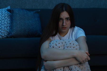 Fear of darkness. Scared young woman with blanket near couch indoors at night, space for textの写真素材