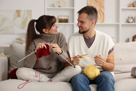 Woman teaching her boyfriend how to knit on sofa at homeの写真素材