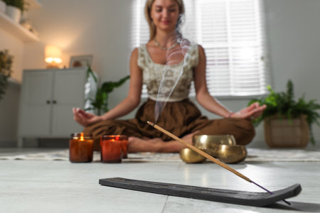 Young woman practicing yoga on floor indoors, focus on smoldering incense stickの写真素材