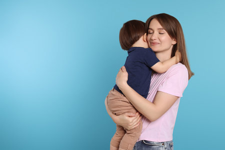 Beautiful mother with her cute little son on light blue background, space for textの写真素材