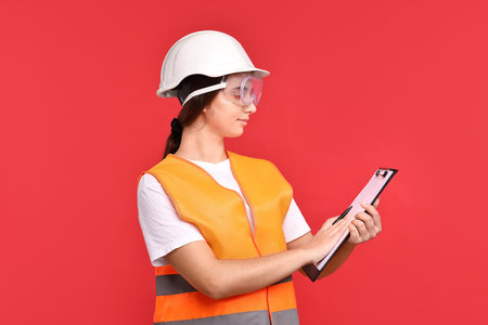 Girl with safety equipment and clipboard on red background. Work for teenagersの写真素材