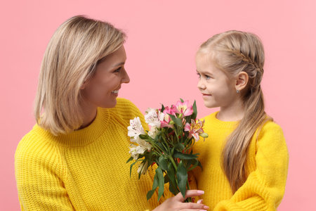 Little daughter congratulating her mom with bouquet of alstroemeria flowers on pink background....