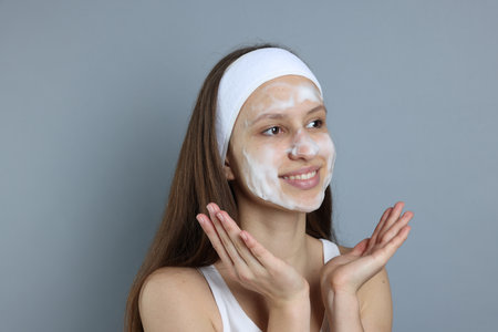 Teenage girl with cleansing foam on her face against grey background. Acne treatmentの写真素材