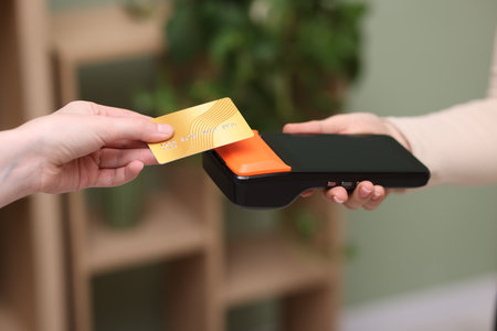 Woman paying with credit card via terminal against blurred background, closeupの写真素材