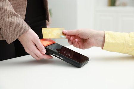 Woman paying for service with credit card via terminal at white table indoors, closeup