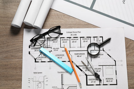 Different engineering drawings, pencil, dividers, ruler, glasses and magnifying glass on wooden table, flat layの写真素材