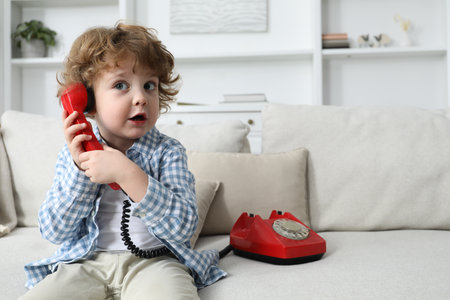 Cute little boy with telephone on sofa indoorsの写真素材