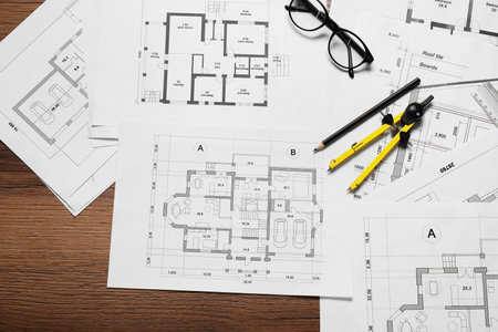 Different architectural drawings, pencil, glasses and divider on wooden table, flat layの写真素材
