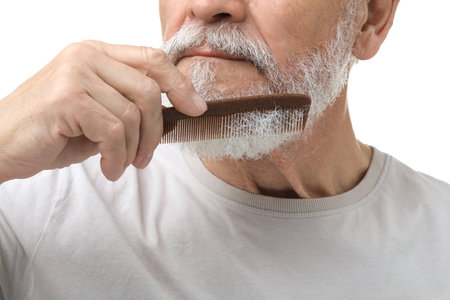 Senior man combing beard on white background, closeup