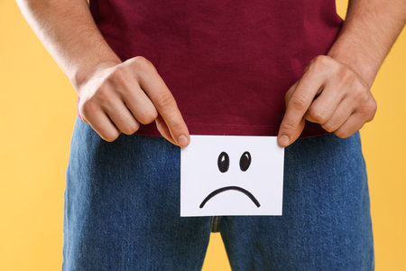 STD (sexually transmitted diseases). Man holding sticky note with drawn sad face on yellow...