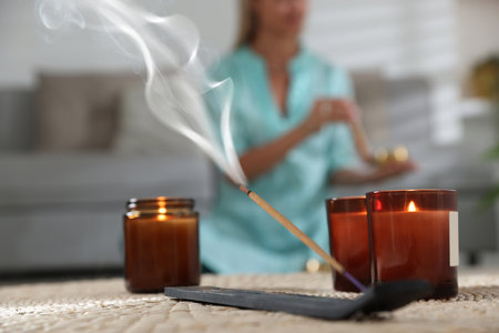 Incense stick smoldering in holder and burning candles on wicker mat indoors, selective focusの写真素材