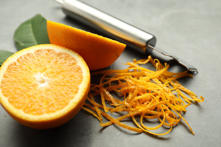 Orange zest, zester tool and fresh fruit pieces on gray textured table, closeupの写真素材