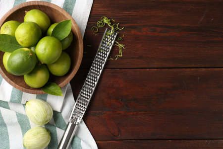Lime zest, grater and fresh fruits on wooden table, flat lay. Space for text