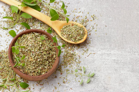 Dried oregano in bowl, spoon and green leaves on light gray table, top view. Space for textの写真素材