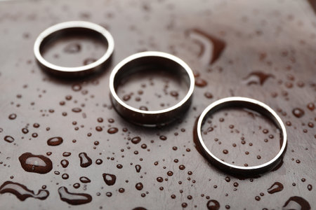 Stylish rings on leather surface with drops, closeup