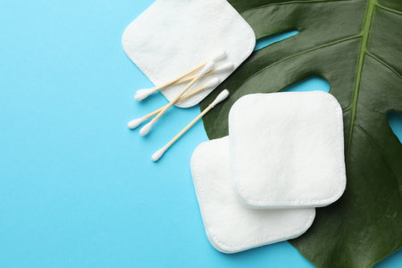 Cotton pads, swabs and monstera leaf on light blue background, flat lay. Space for textの写真素材